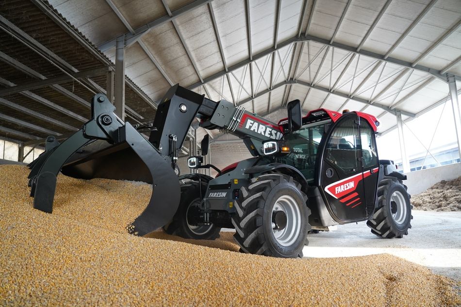 Ein Traktor mit Schippe, hebt Tierfutter in einer Scheune an