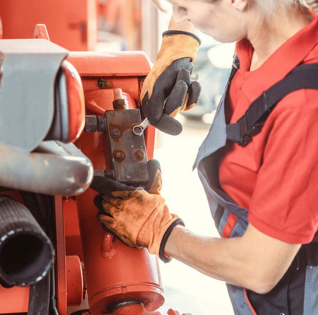 Eine Frau in Arbeitskleidung montiert an einer Landmaschine ein Ersatzteil